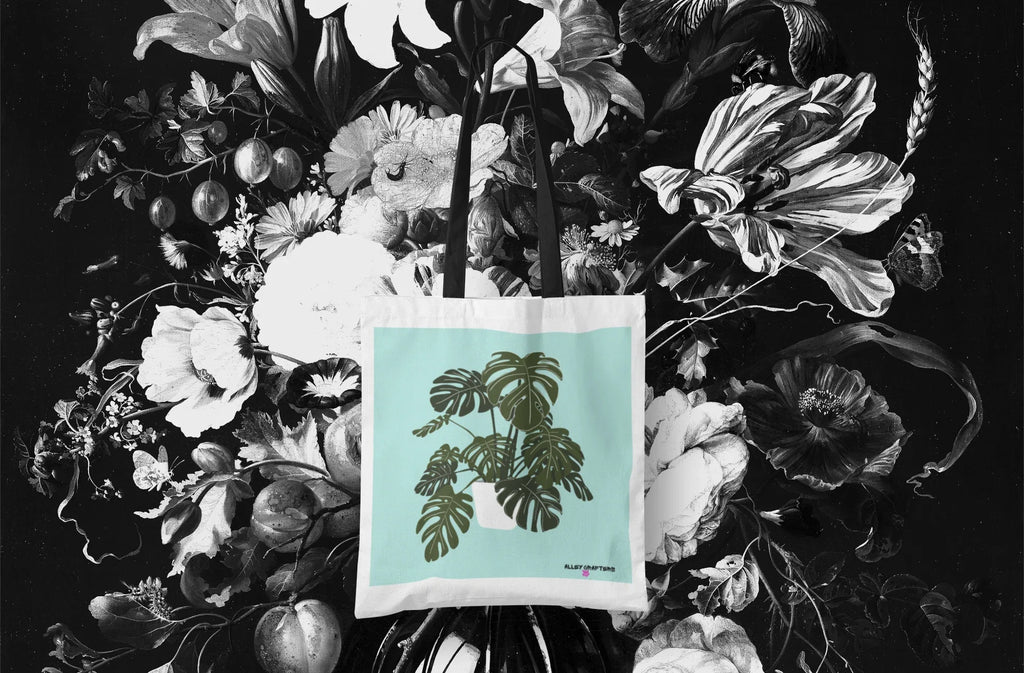 White tote bag with black handles and green monstera leaf artwork