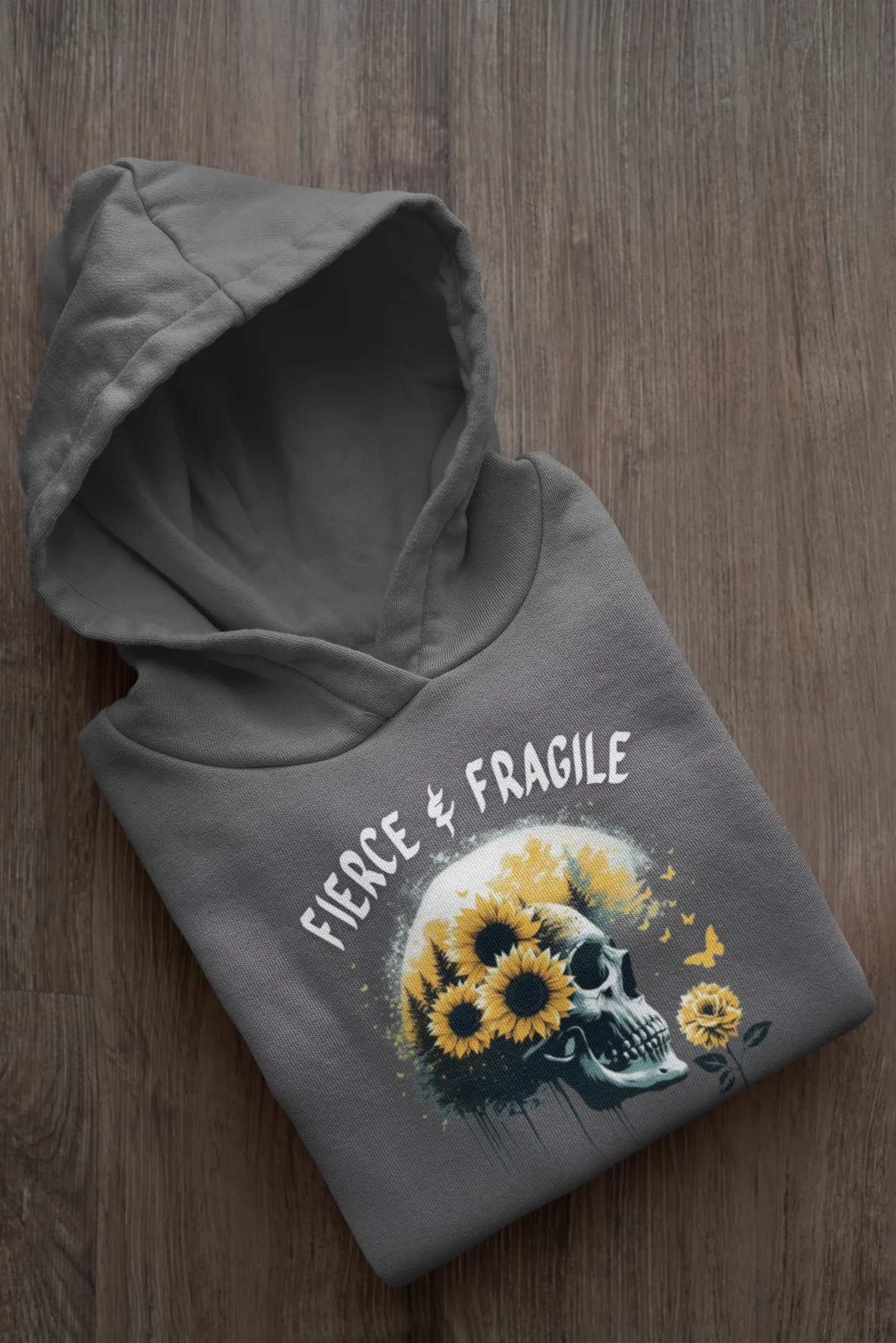 Charcoal gray hooded sweatshirt folded on wood, with sunflower skull graphic