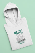 White pullover hoodie with green nature mountain “Best Medicine” graphic, folded view.