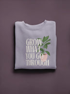 White crewneck sweatshirt with “Grow What You Go Through” graphic and green leaf