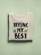Light cream crewneck sweatshirt with 'TRYING MY BEST' graphic text and leaf icons