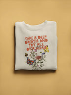 White crewneck sweatshirt with floral quote graphic, folded flat on display