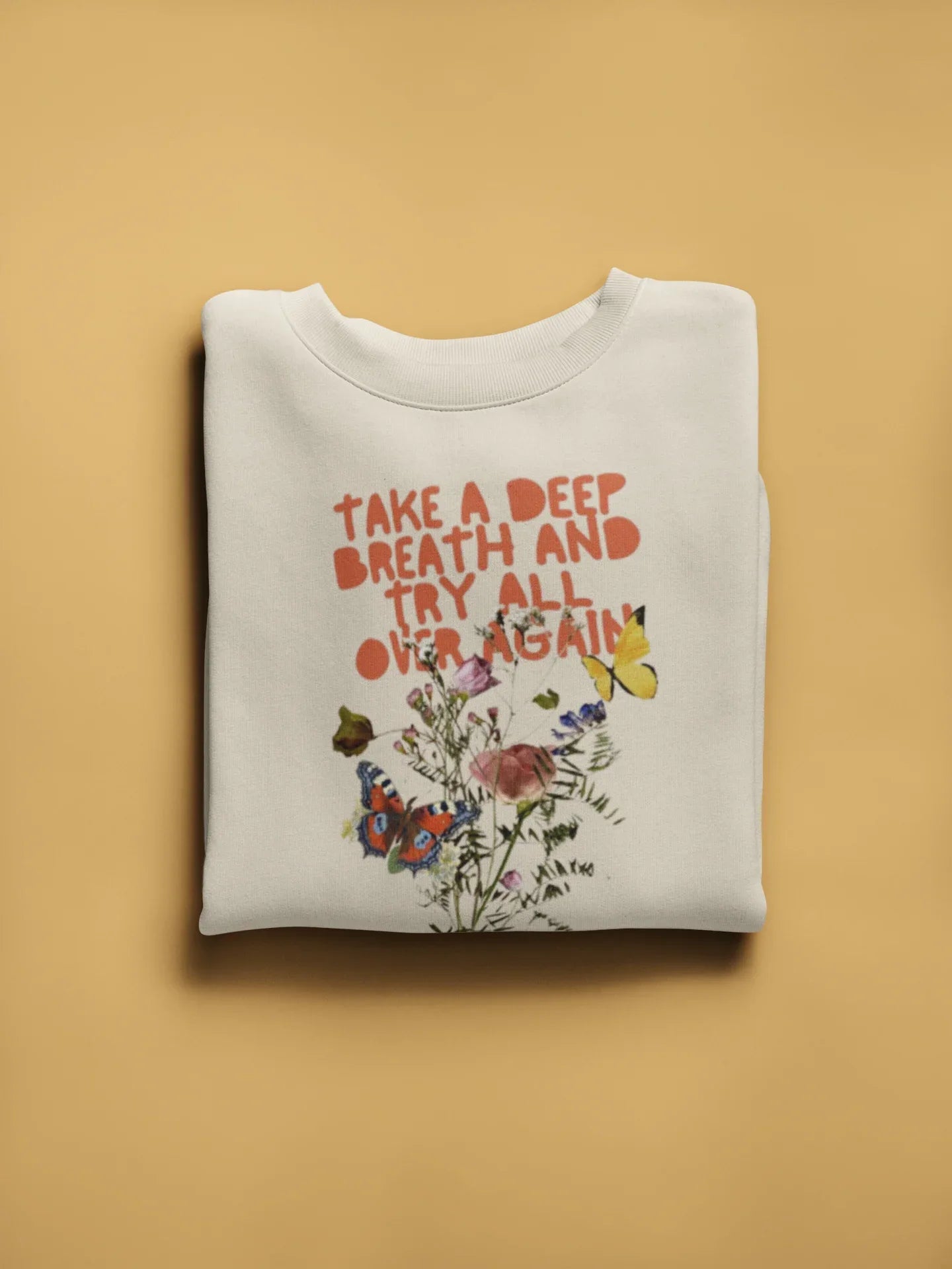 White crewneck sweatshirt with floral quote graphic, folded flat on display