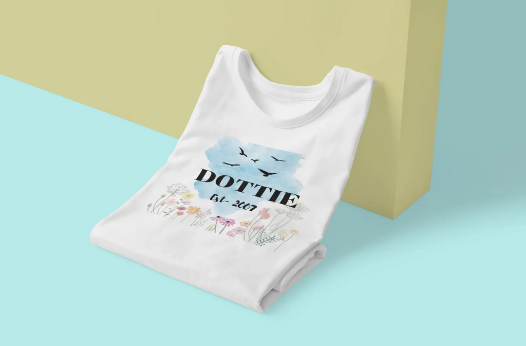 Folded white T-shirt, blue birds and floral name/year graphic.