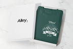 Folded green crewneck sweatshirt with centered chest adventure graphic