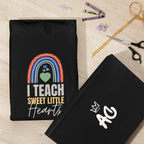 Black unisex hoodie with front “I TEACH SWEET LITTLE Hearts” graphic; shown with folded sleeve