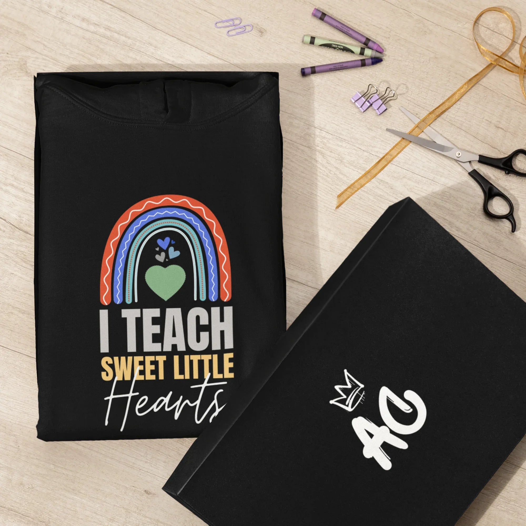 Black unisex hoodie with front “I TEACH SWEET LITTLE Hearts” graphic; shown with folded sleeve