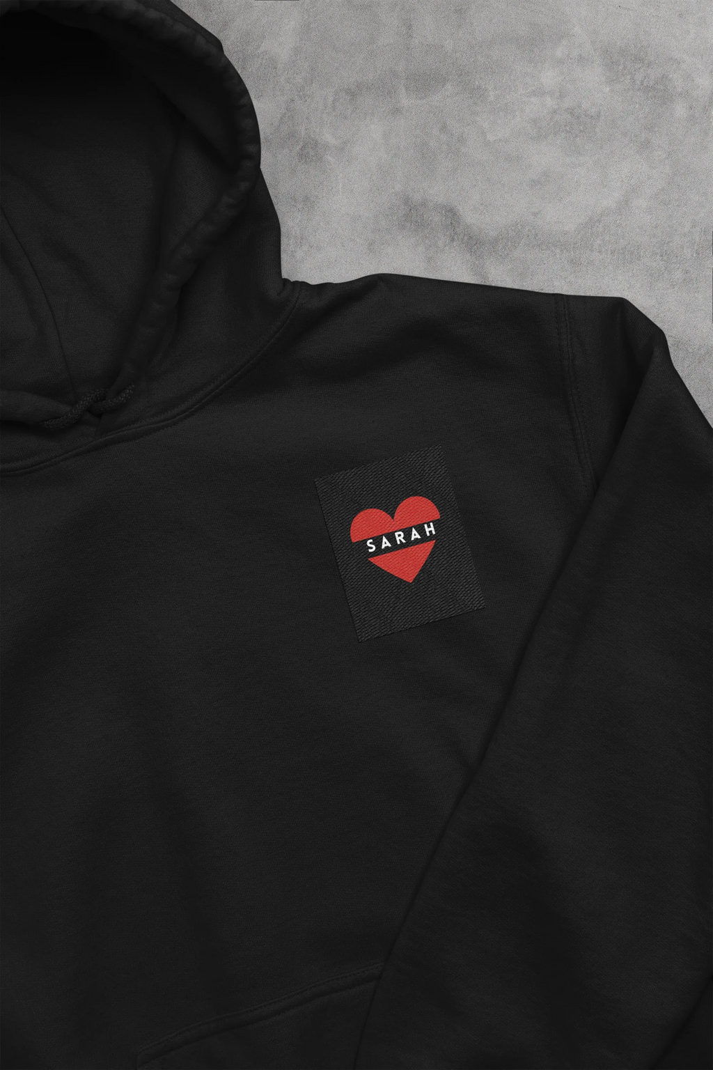 Black unisex hoodie with heart embroidery name patch reading SARAH