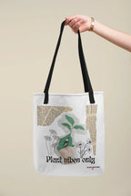 White tote bag with black handles and green plant graphic, held overhead
