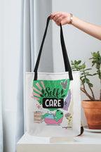 White tote bag with black handles featuring “Self Care” and green frog illustration