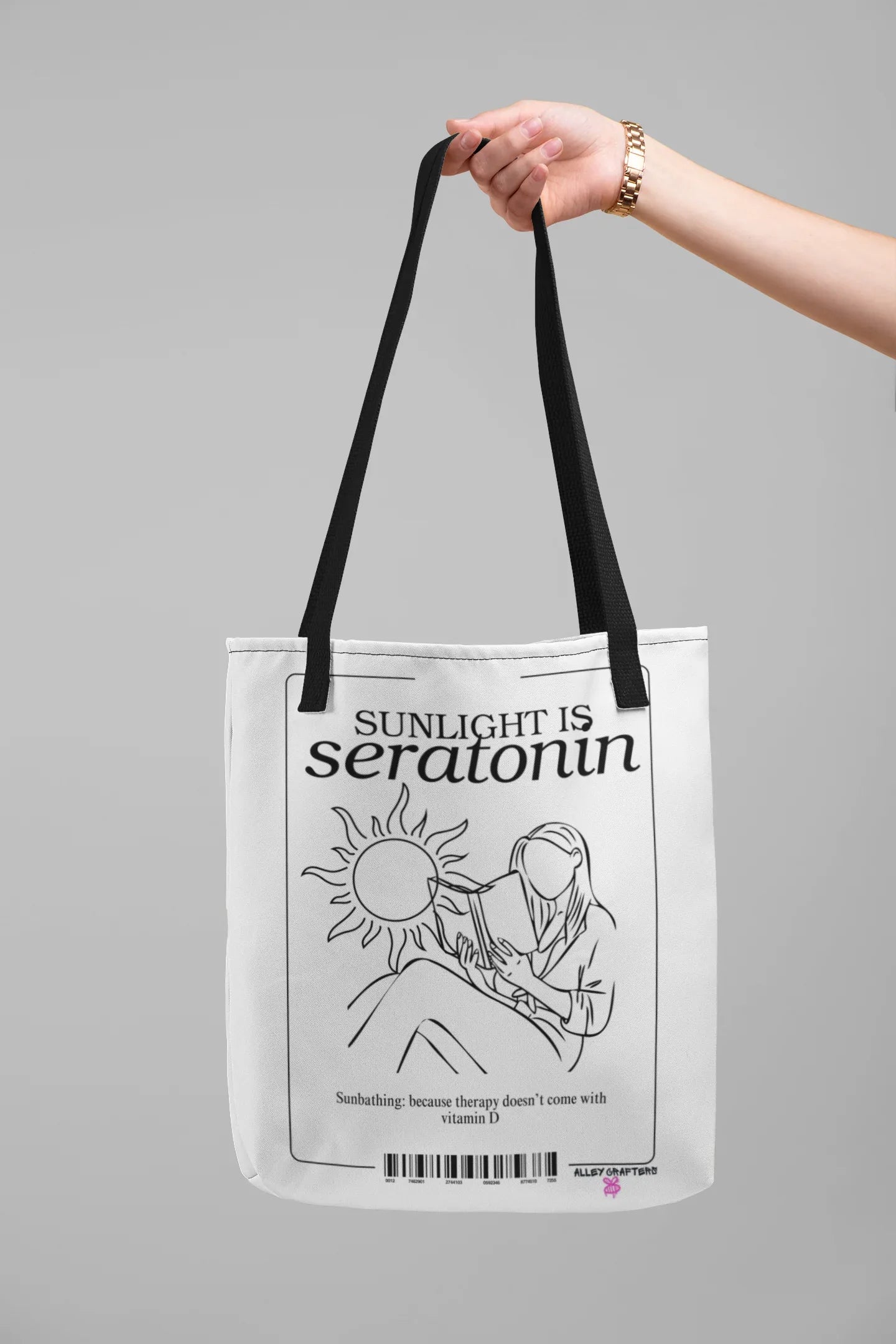 White canvas tote bag held by handles, showing black front text and illustration