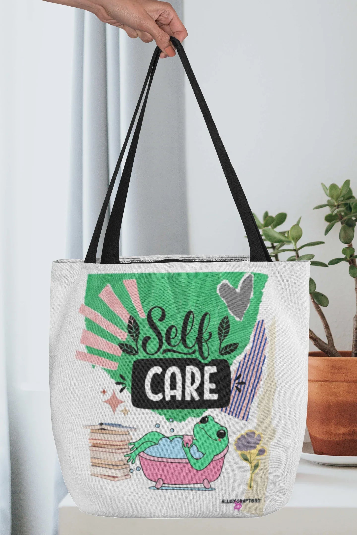 White tote bag with black handles and “Self Care” graphic with green frog