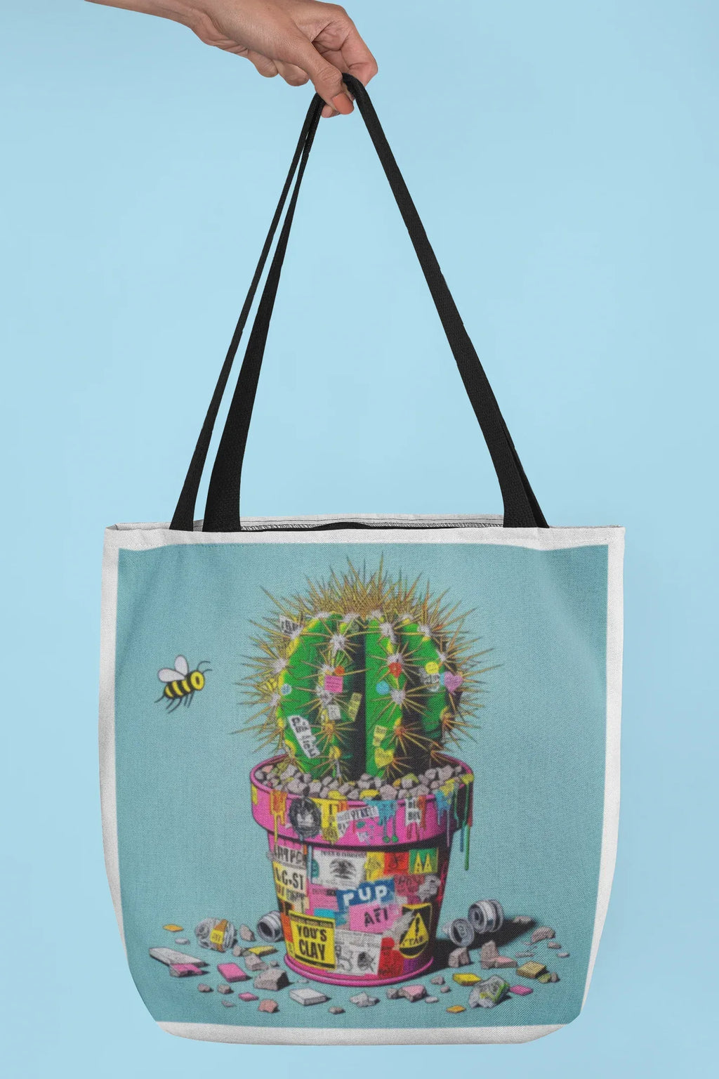 Tote bag with cactus artwork, light blue panel, black handles, held up