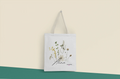 White canvas tote bag with black handle straps and botanical flower graphic front