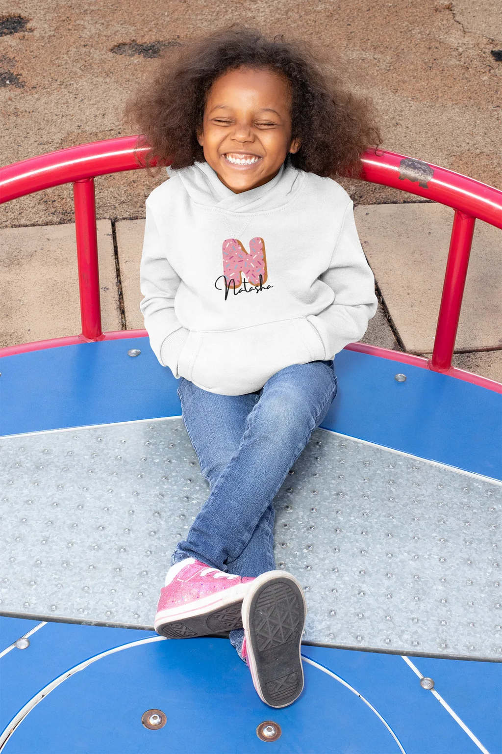 White kids hoodie with hood, front pocket, and pink donut graphic on the chest.