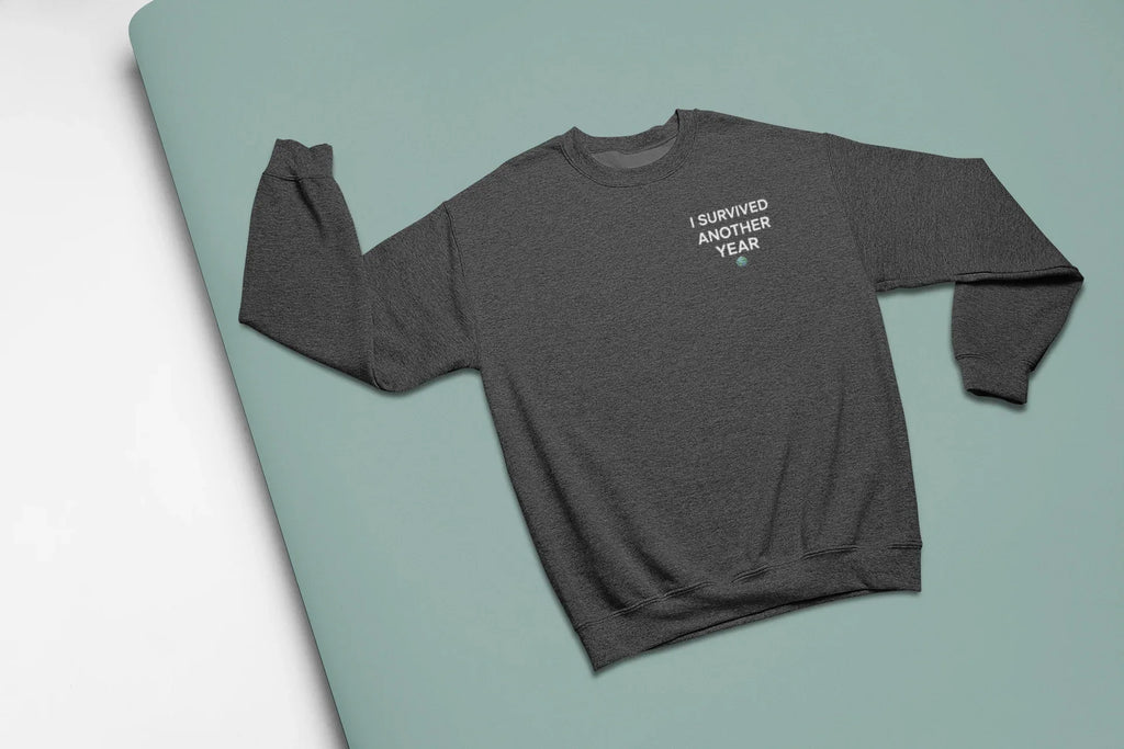 Gray heather crewneck sweatshirt with front text graphic “I SURVIVED ANOTHER YEAR”