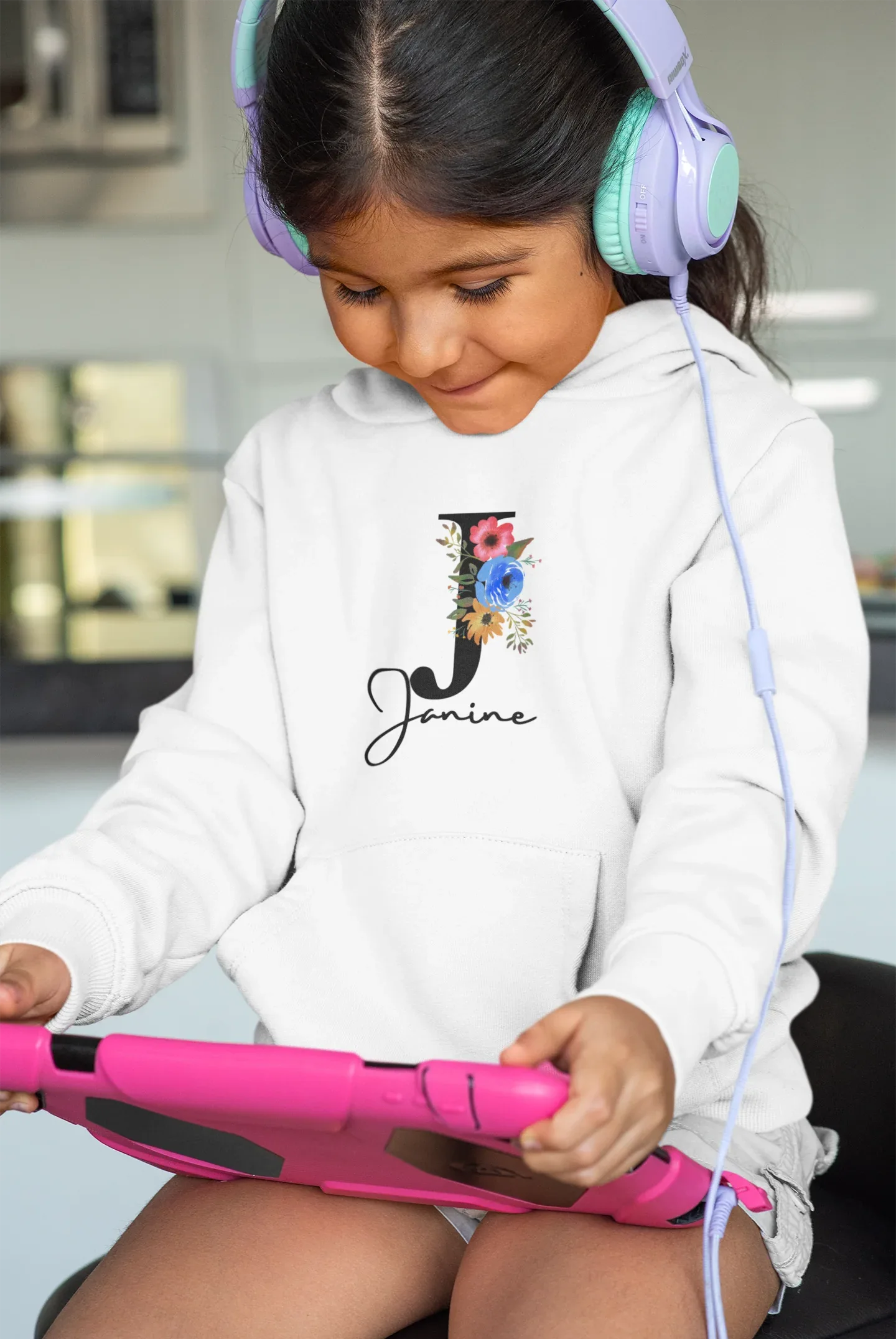 White kids hoodie on a child wearing headphones, floral letter and script name on chest