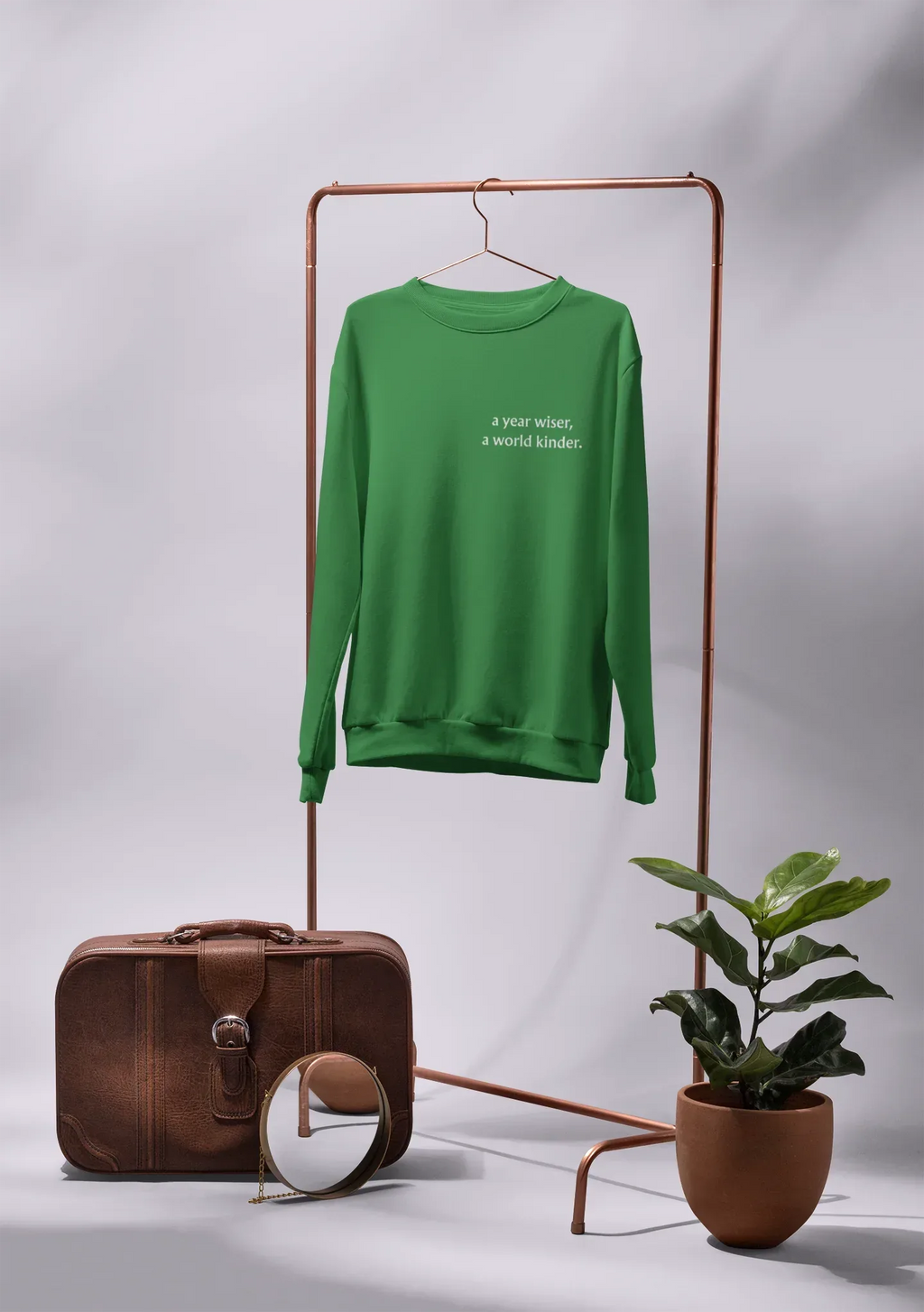 Green crewneck sweatshirt on hanger with 'a year wiser, a world kinder.' print