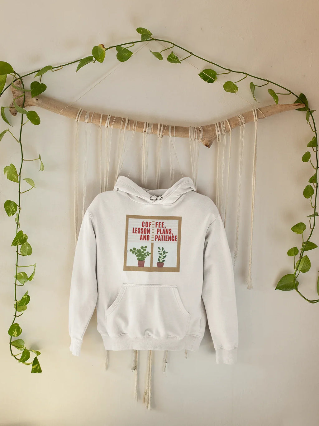 White pullover hoodie hanging with hood and pouch pocket, showing potted plant graphic on front