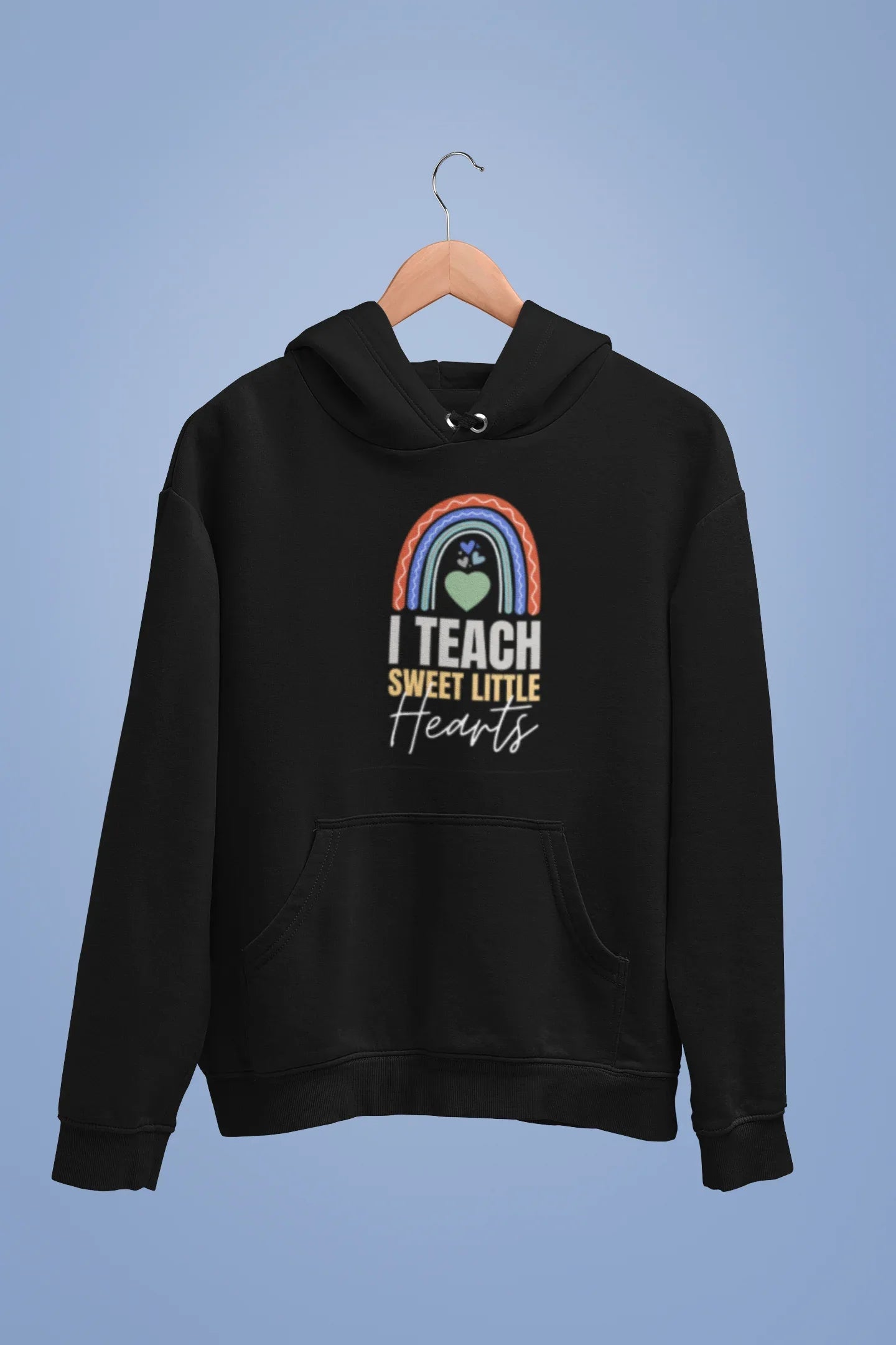 Black unisex hoodie on hanger with front pocket and chest graphic: rainbow heart “I TEACH”