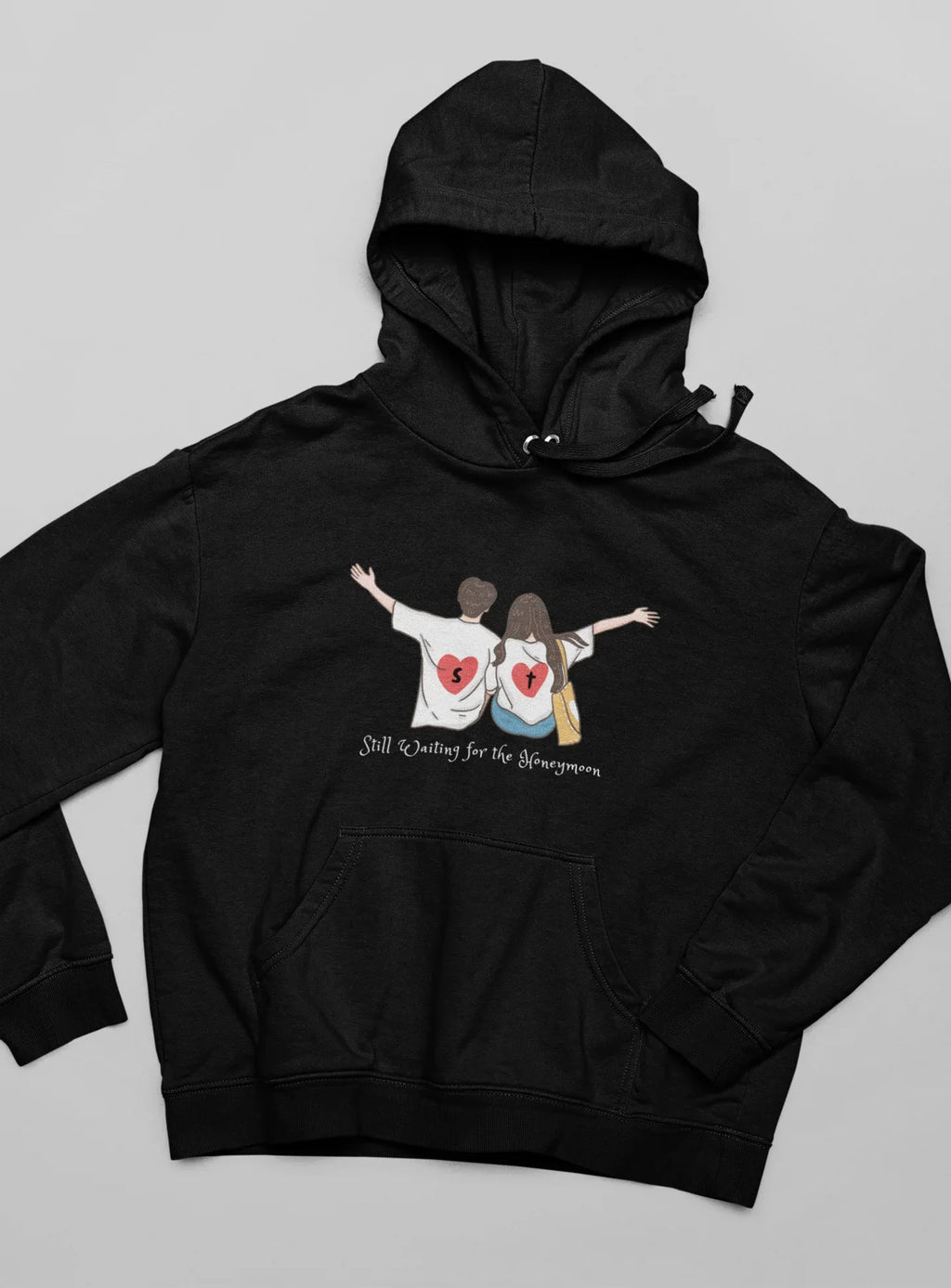 Black zip-less hoodie with drawstring and couple heart graphic on front.