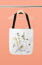 White canvas tote bag with black handle straps and botanical flower print front