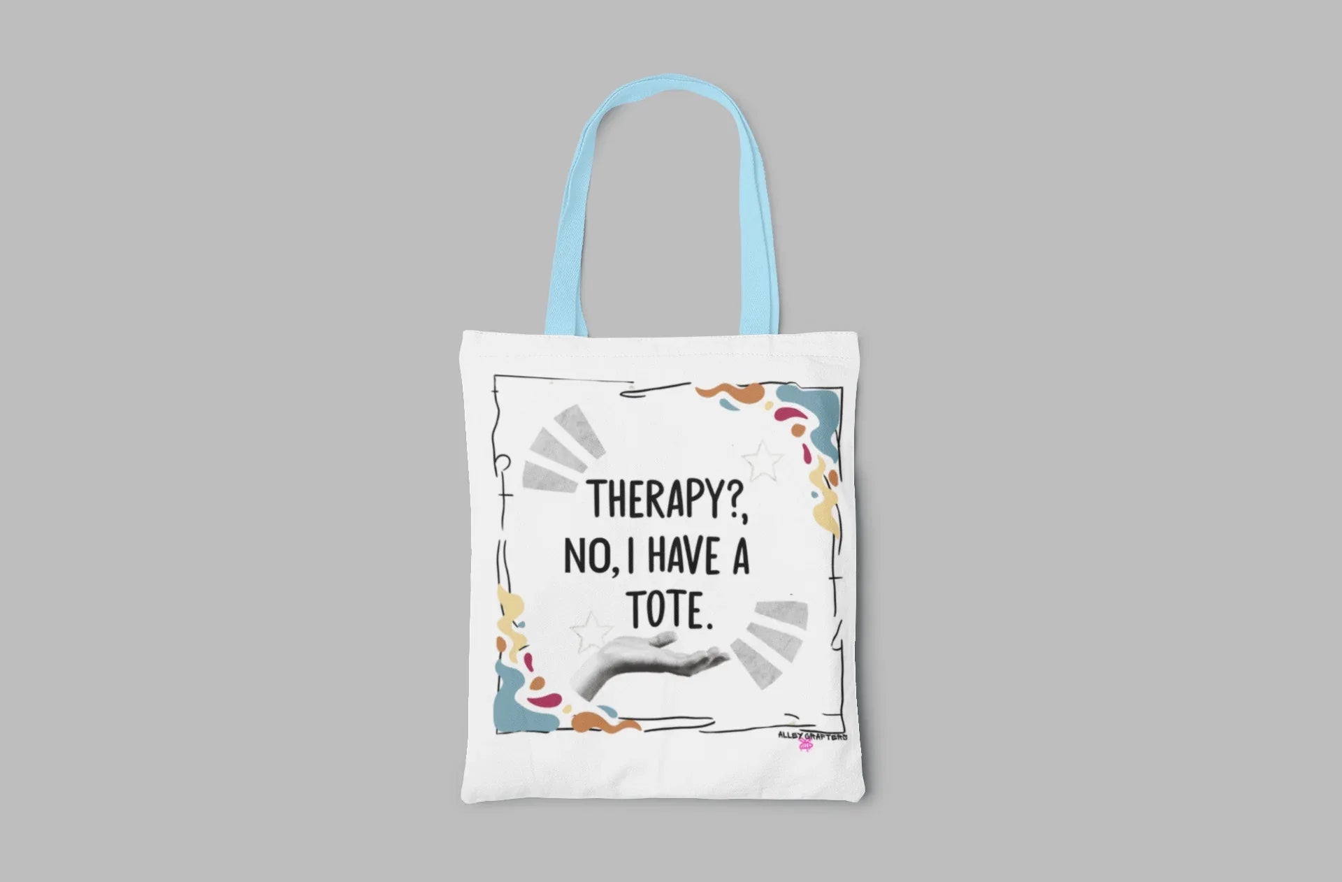 White tote bag with “Therapy?, No, I have a Tote” print and colorful border, light blue handles