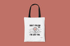 White tote bag with black "DON'T FOLLOW ME" text and red location-pin graphic