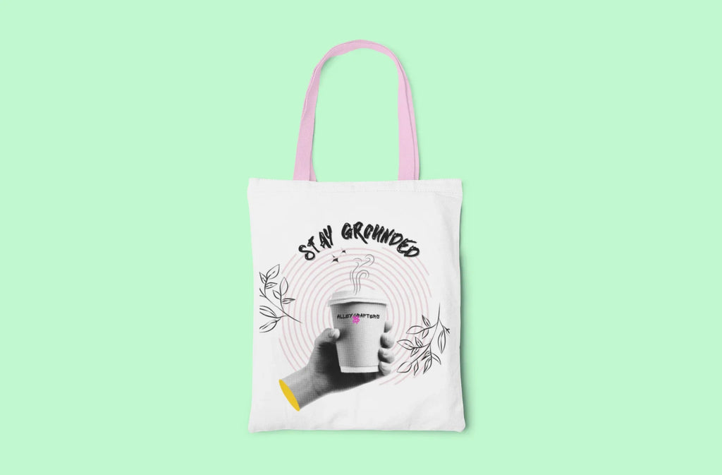 White canvas tote bag with pink handles and Stay Grounded coffee cup graphic