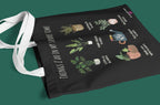 Black tote bag flat-lay with white handles and plant collage text 'THINGS I DO IN MY SPARE TIME'.