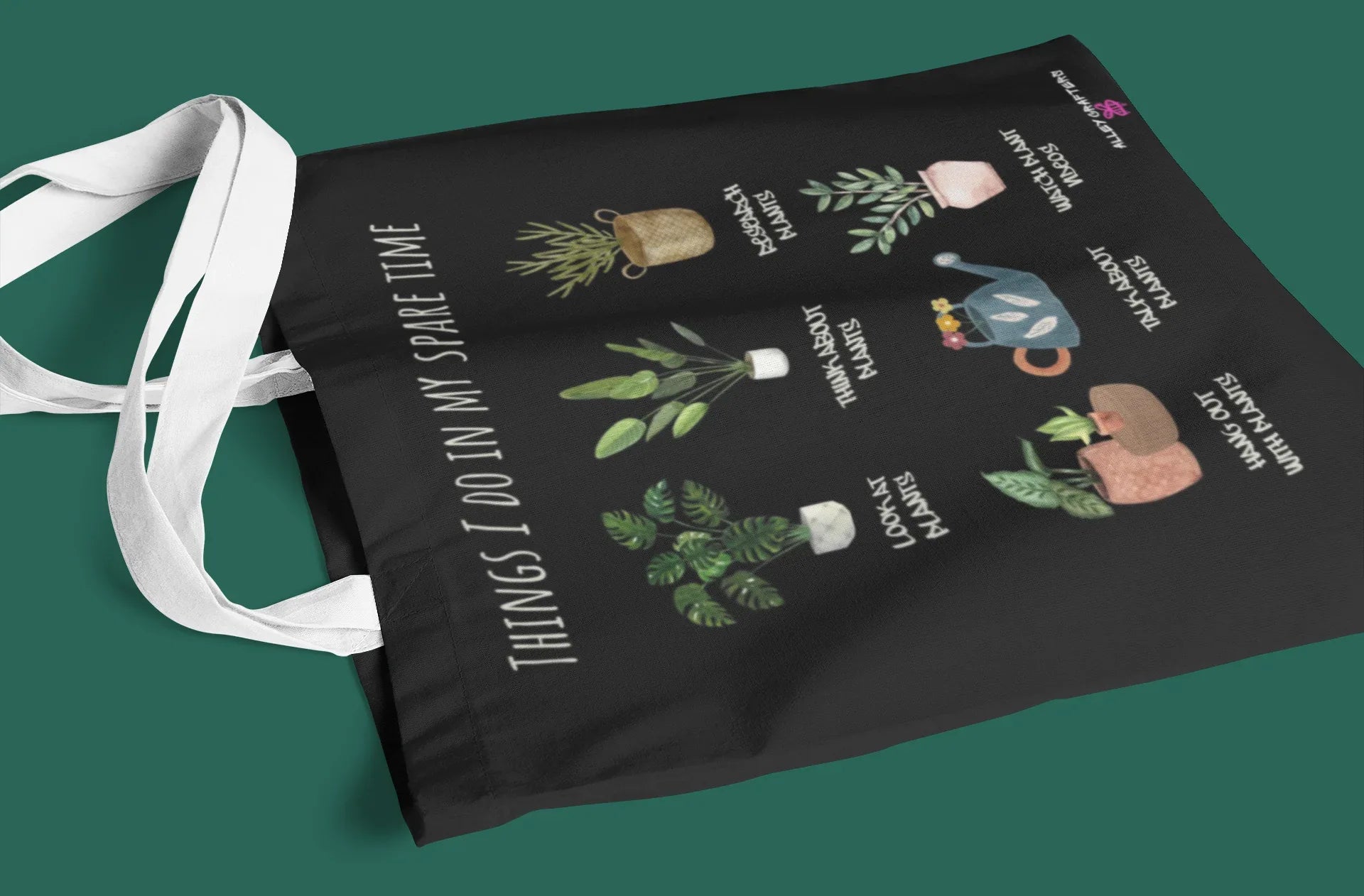 Black tote bag flat-lay with white handles and plant collage text 'THINGS I DO IN MY SPARE TIME'.