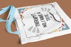 White tote bag with “Therapy?, No, I have a Tote” text and colorful border, light strap