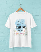 Hanging white T-shirt, blue birds and floral design with name and year.