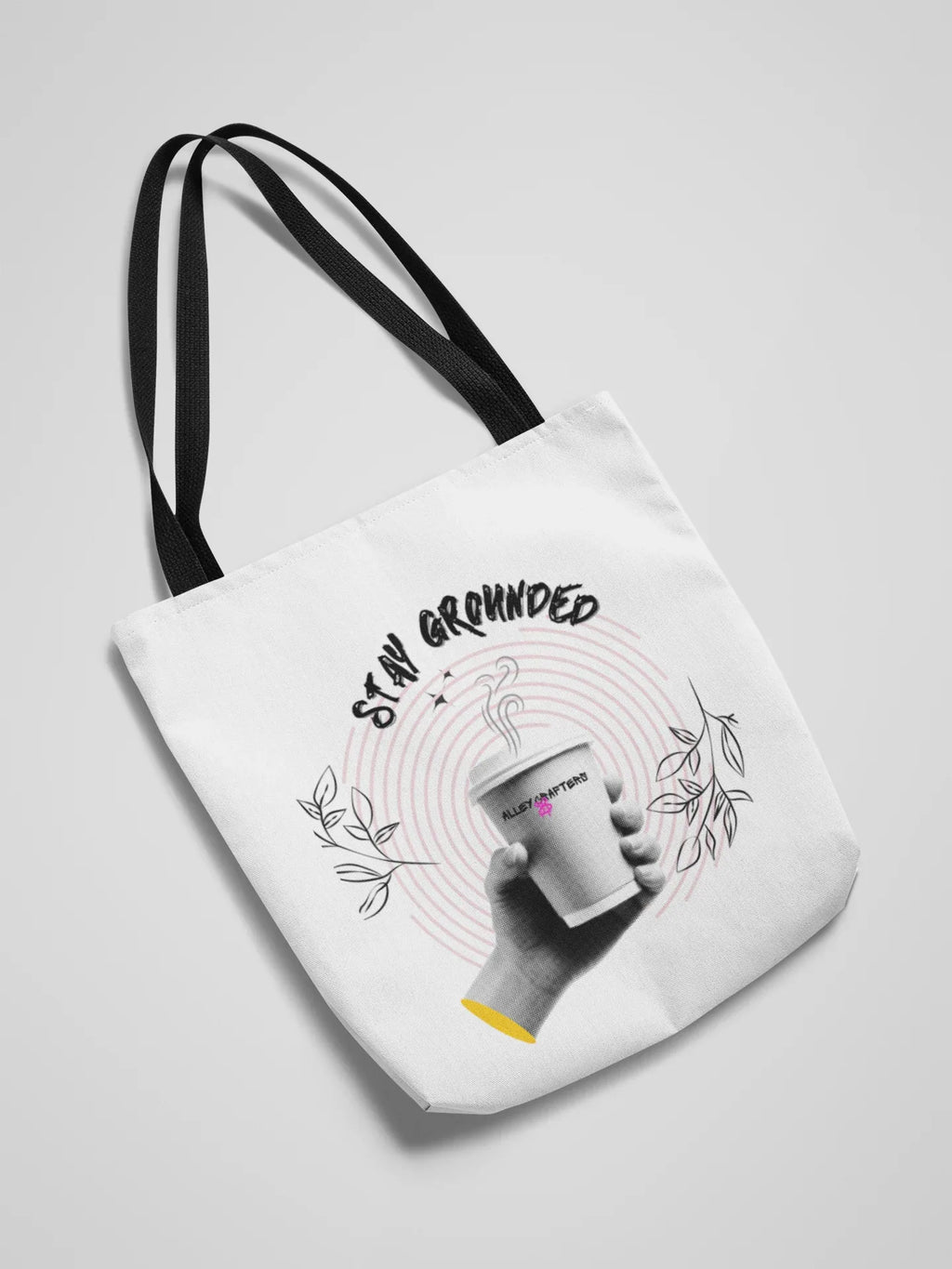 White canvas tote bag with black handles and Stay Grounded coffee graphic