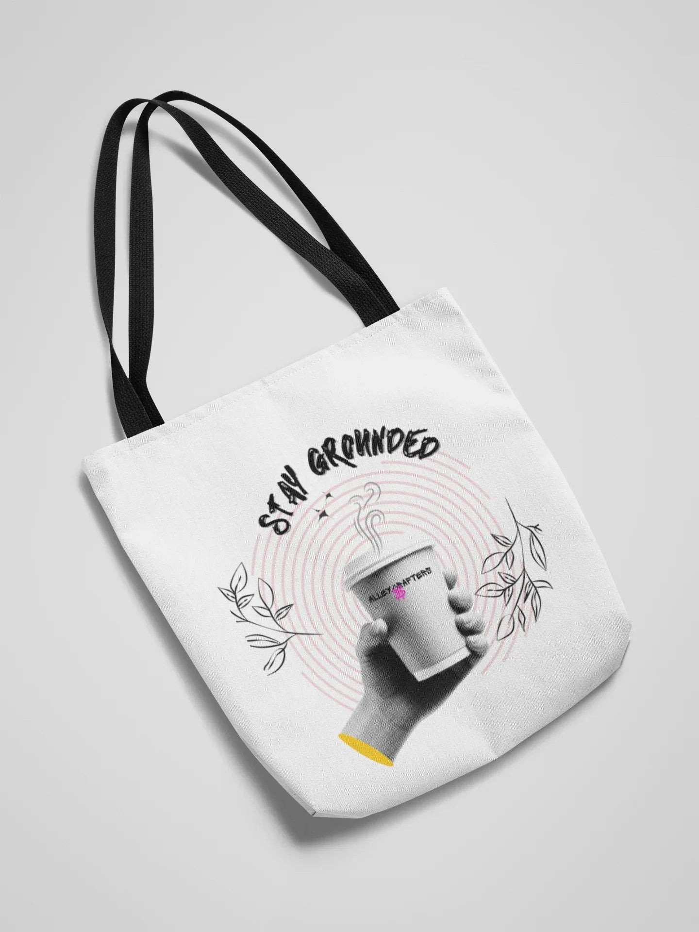 White canvas tote bag with black handles and Stay Grounded coffee graphic