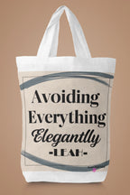 White canvas tote bag with large "Avoiding Everything Elegantly" lettering