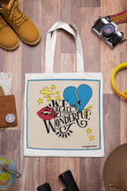 Light canvas tote bag with black handles and front graphic on a wooden surface