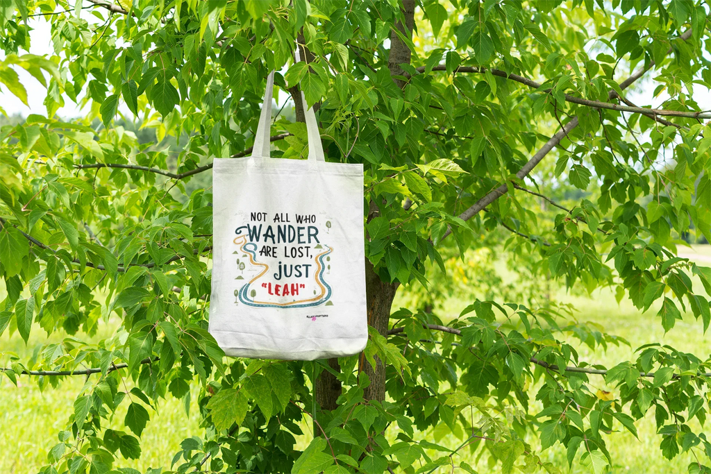 White canvas tote bag with long handles, colorful “wander” quote centered on front