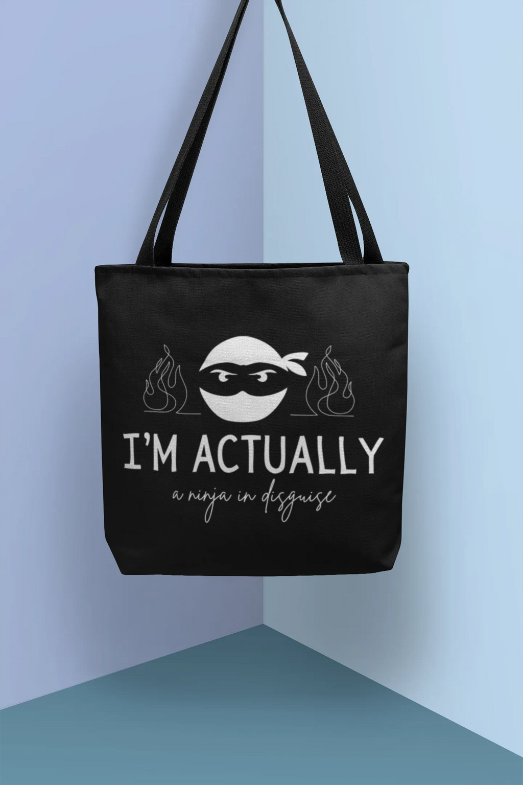 Black tote bag with handles and ninja face graphic, 'I'M ACTUALLY' and 'a ninja in disguise'.