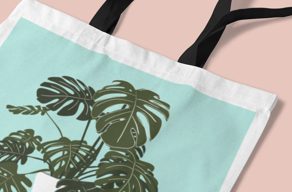 Close-up of white tote bag with green monstera leaf print and striped edge