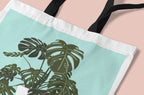 Close-up of white tote bag with green monstera leaf print and striped edge