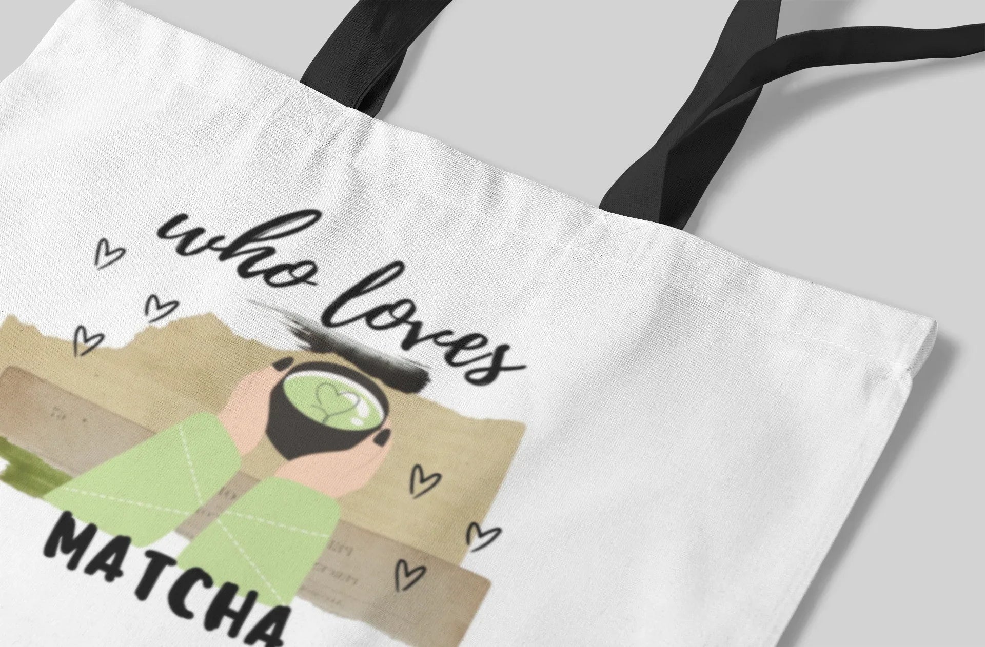 White tote bag corner close-up showing “who loves MATCHA” text and hearts.