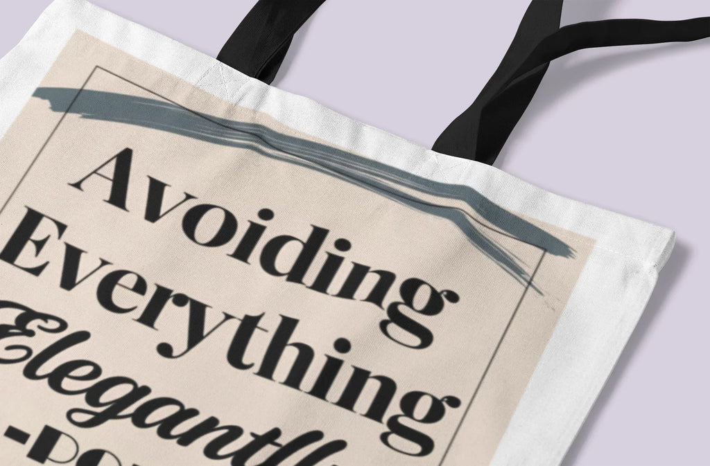 White canvas tote bag close-up with “Avoiding Everything Elegantly” printed in dark