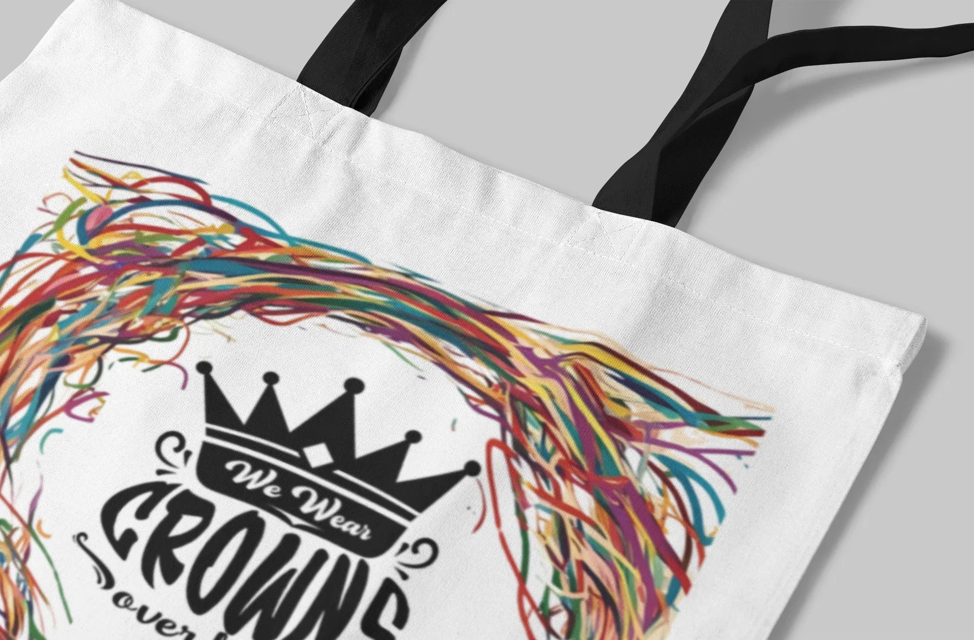 White tote bag close-up: multicolor scribble wreath around black crown logo