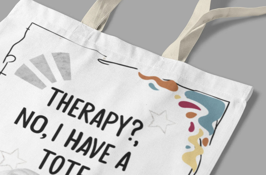 Close-up of white tote bag print with “THERAPY? NO, I HAVE A TOTE.” and doodles.