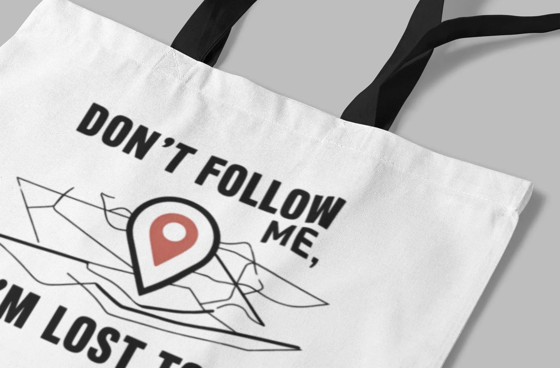 Close-up of white tote bag with black "DON'T FOLLOW ME" text and red map-pin graphic