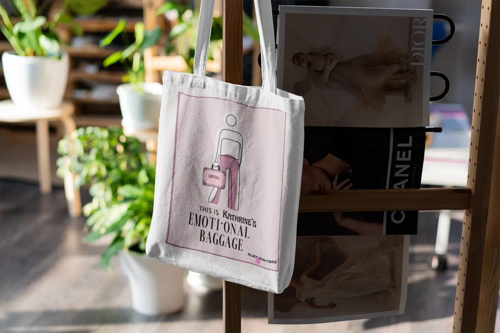 White canvas tote bag hanging with pink graphic design on the front.