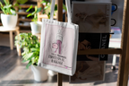 White canvas tote bag hanging with pink graphic design on the front.