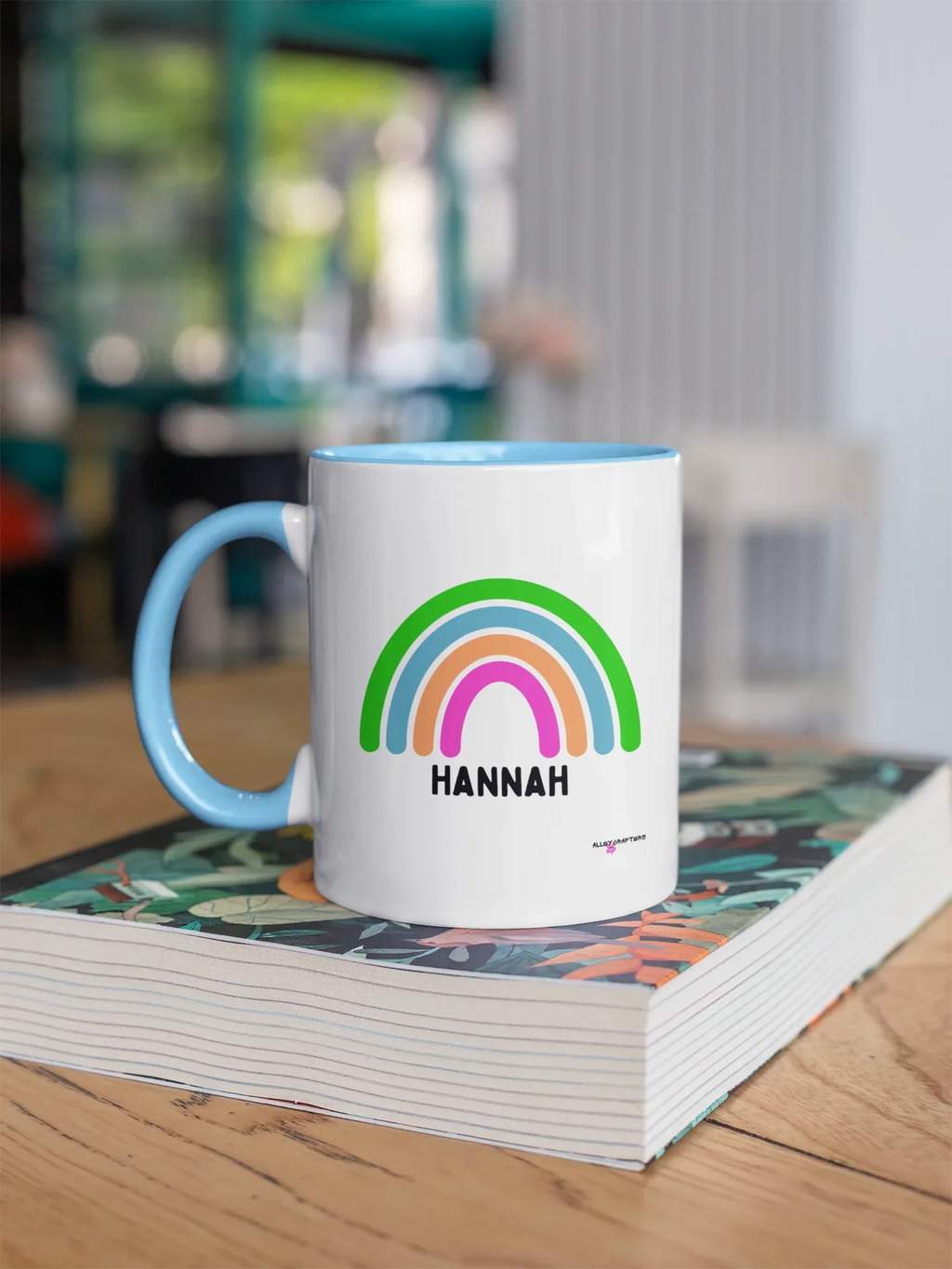 Personalised rainbow mug with HANNAH name, white body and light blue handle, rainbow graphic