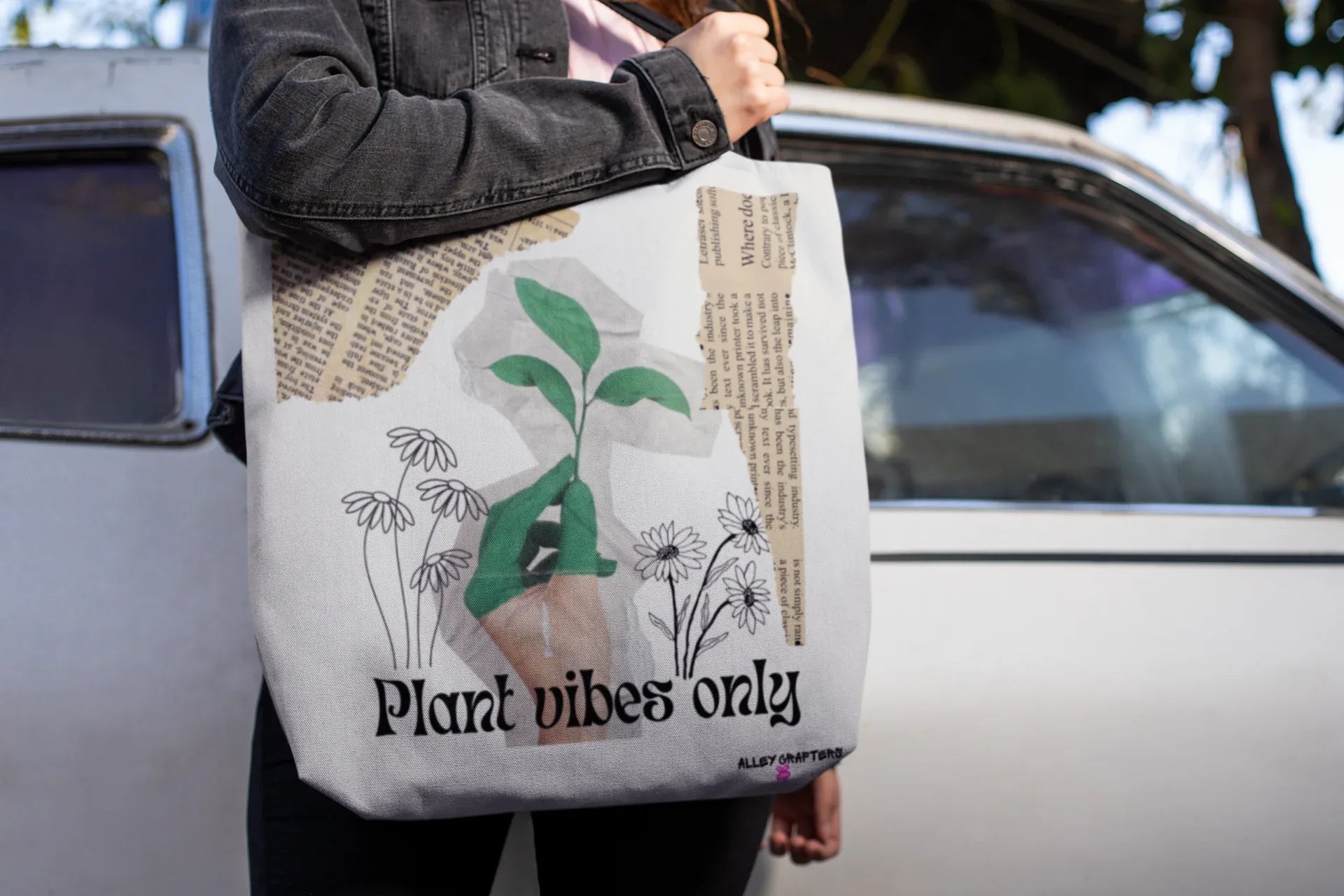 White tote bag with green plant artwork and 'Plant vibes only' logo, held by hand
